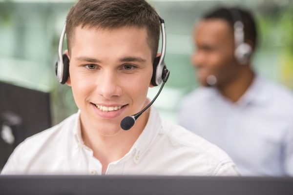 Call center Agent smiling while working on his computer with colleague next to him.